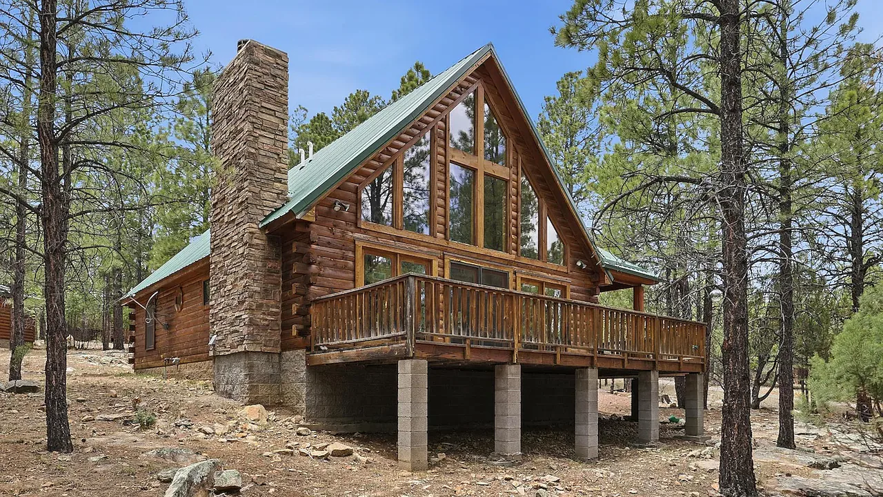 Photo of a log cabin home with a metal roof standing among ponderosa pines in the Flagstaff, Arizona high country